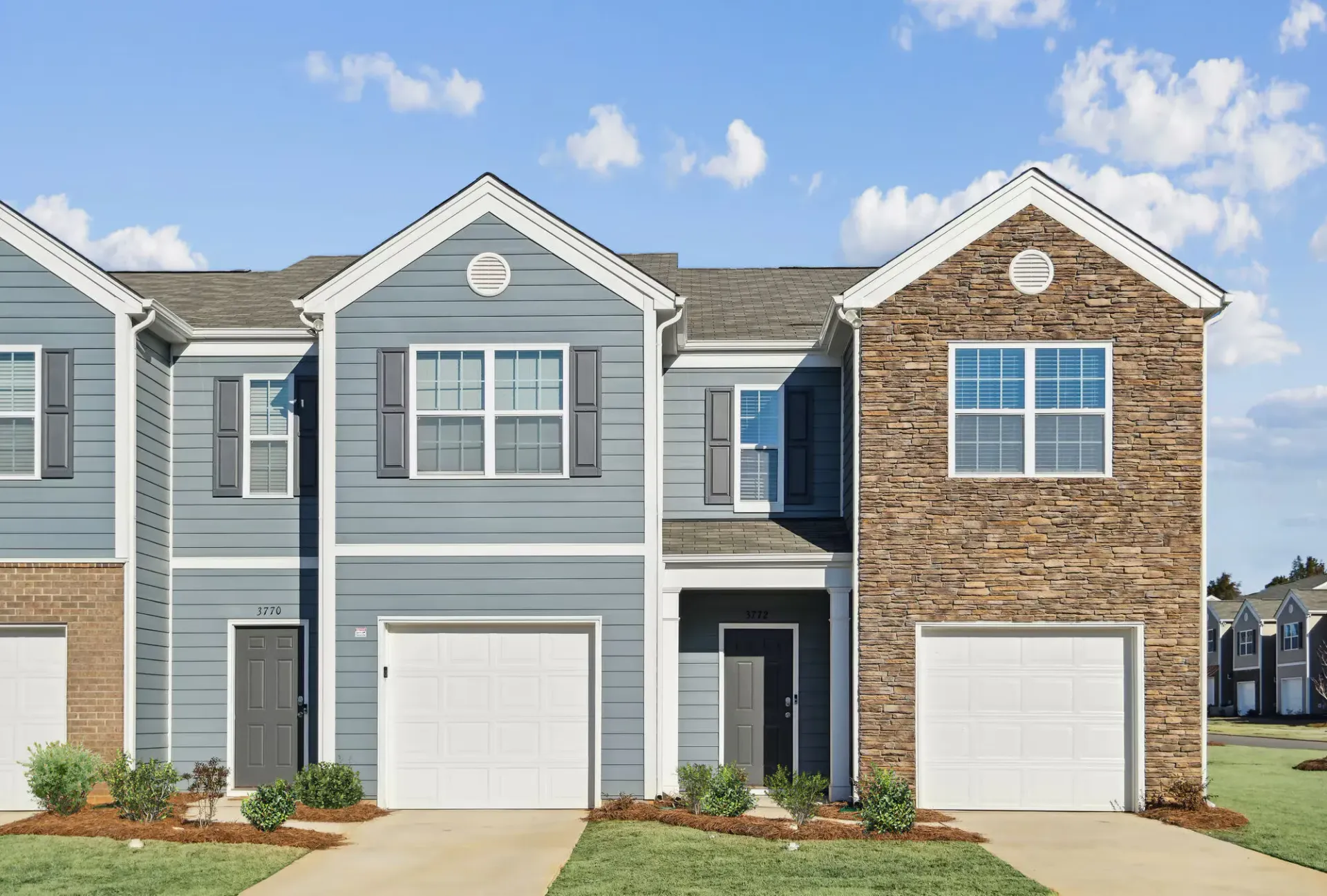 Exterior view of a row of modern townhomes with attached garages and stone accents.