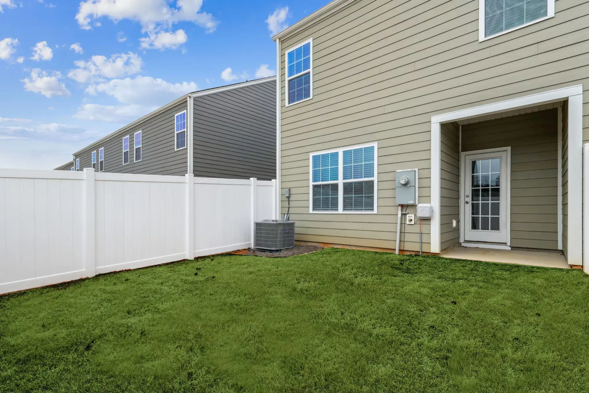 Backyard of a townhouse with beige siding, a white privacy fence, and a back door.