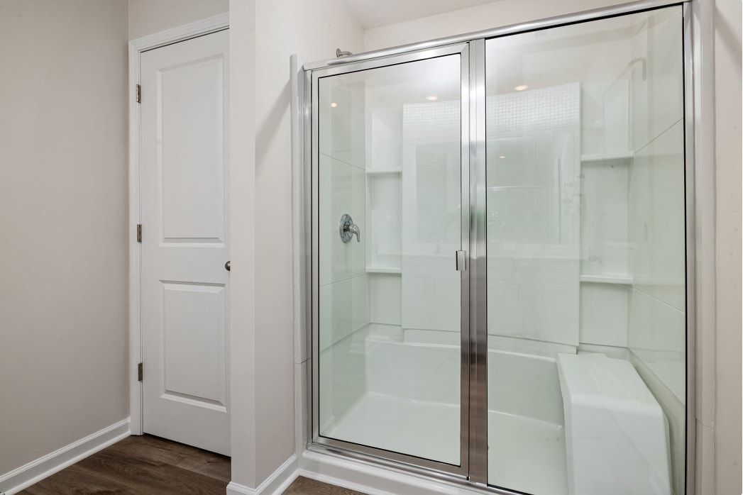 Glass-enclosed shower with a chrome frame in a white bathroom, featuring built-in shelves.