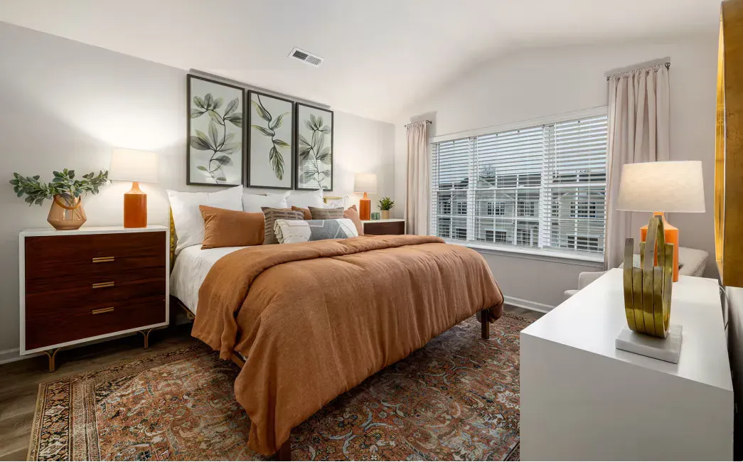 Modern bedroom in an apartment with a large bed, brown bedding, two nightstands, and a window with blinds.
