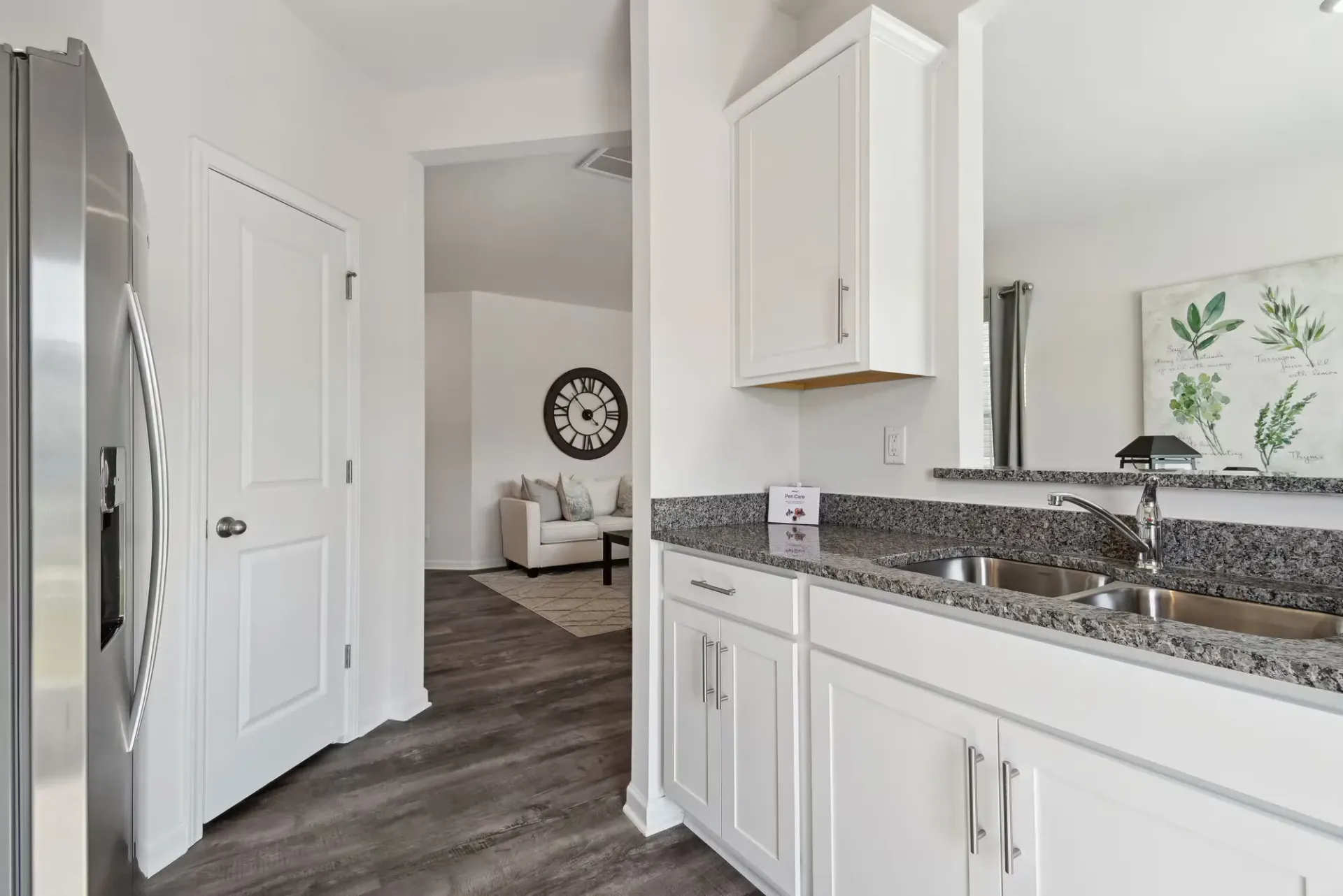 White kitchen with granite countertops, stainless steel fridge, and open view to living area.