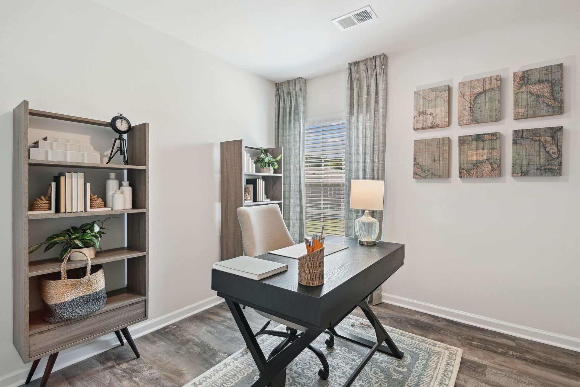 Home office in an apartment with a dark desk, beige chair, shelves, and map wall art.