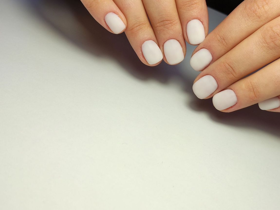 Mani con unghie bianche e curate appoggiate su una superficie chiara
