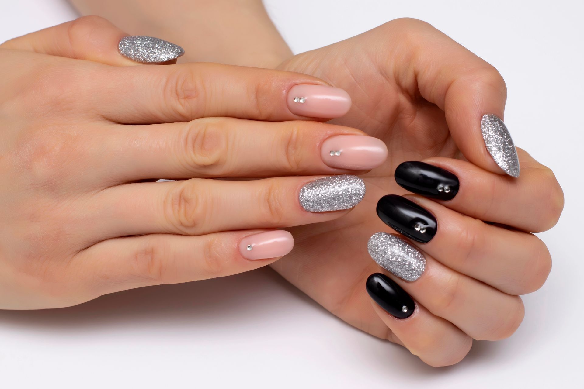Mani con manicure nera, color carne e glitter argento su sfondo bianco