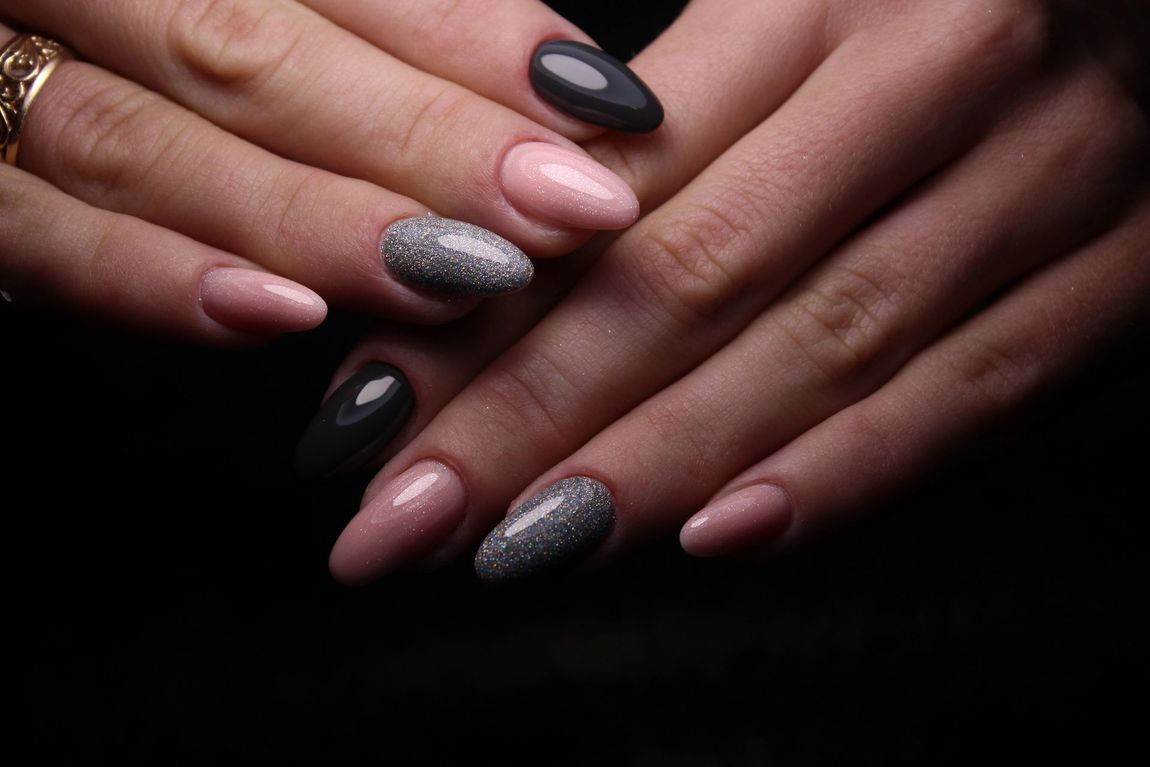 Mani con unghie curate nere, rosa e argento su sfondo scuro