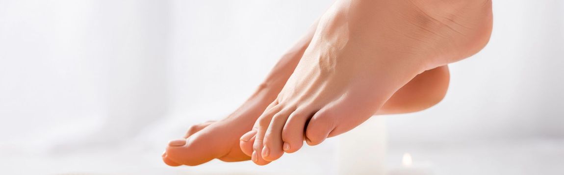 Piedi nudi e mani che si toccano le dita dei piedi durante un esercizio di yoga su sfondo bianco.