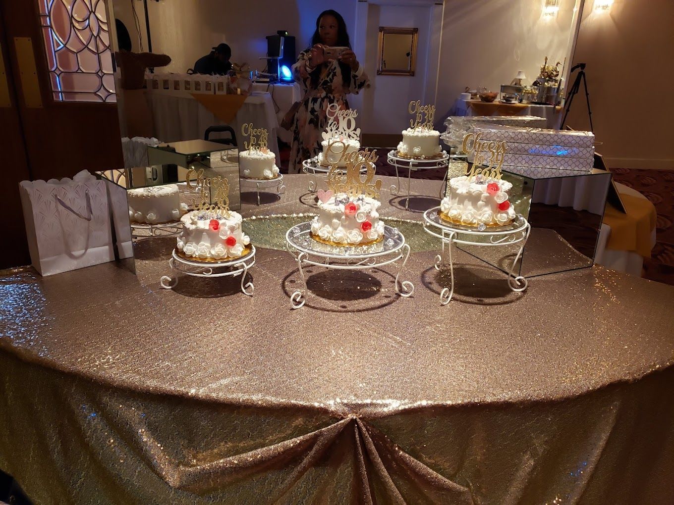 A table with three cakes on it and a woman taking a picture