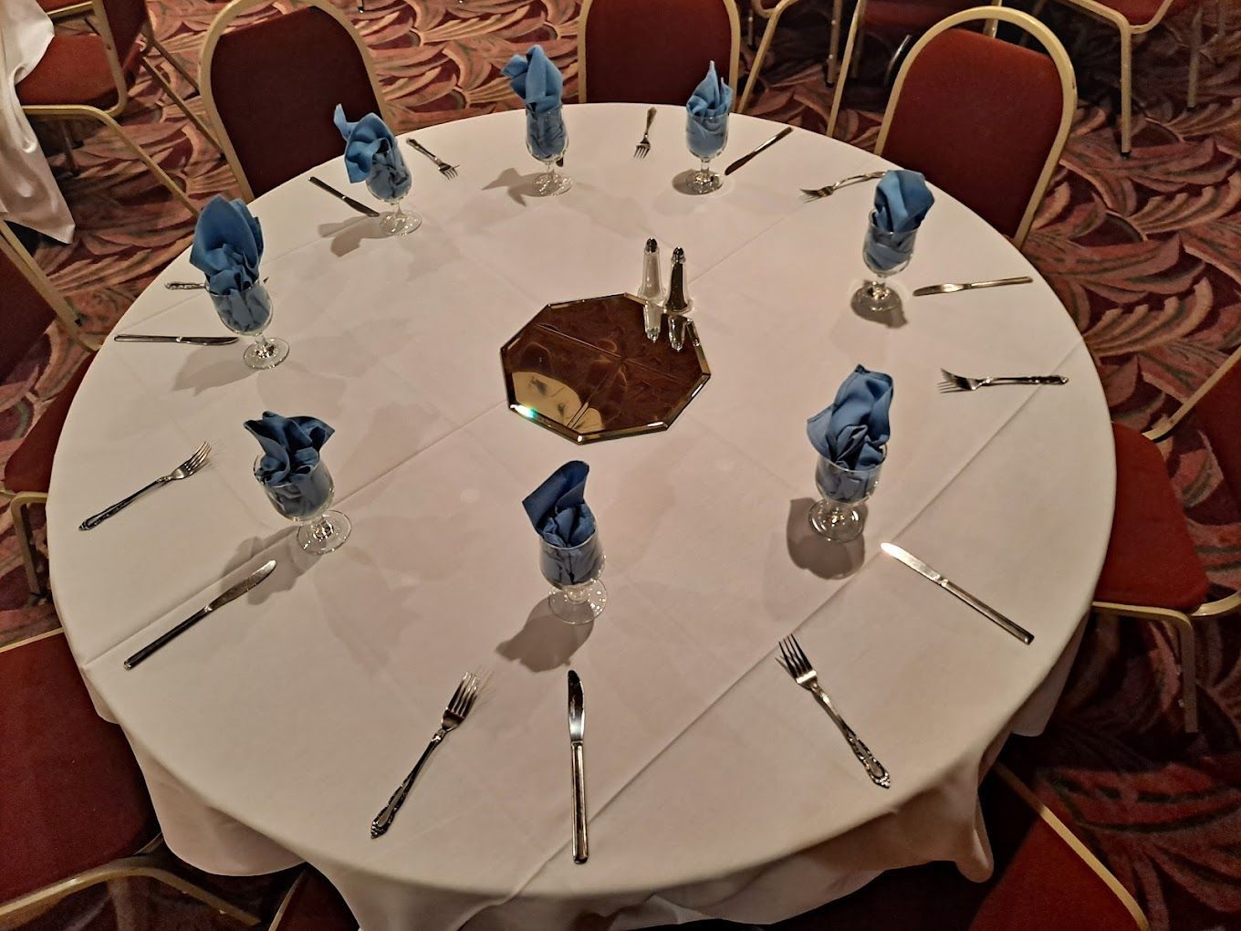 A round table with silverware and blue napkins on it