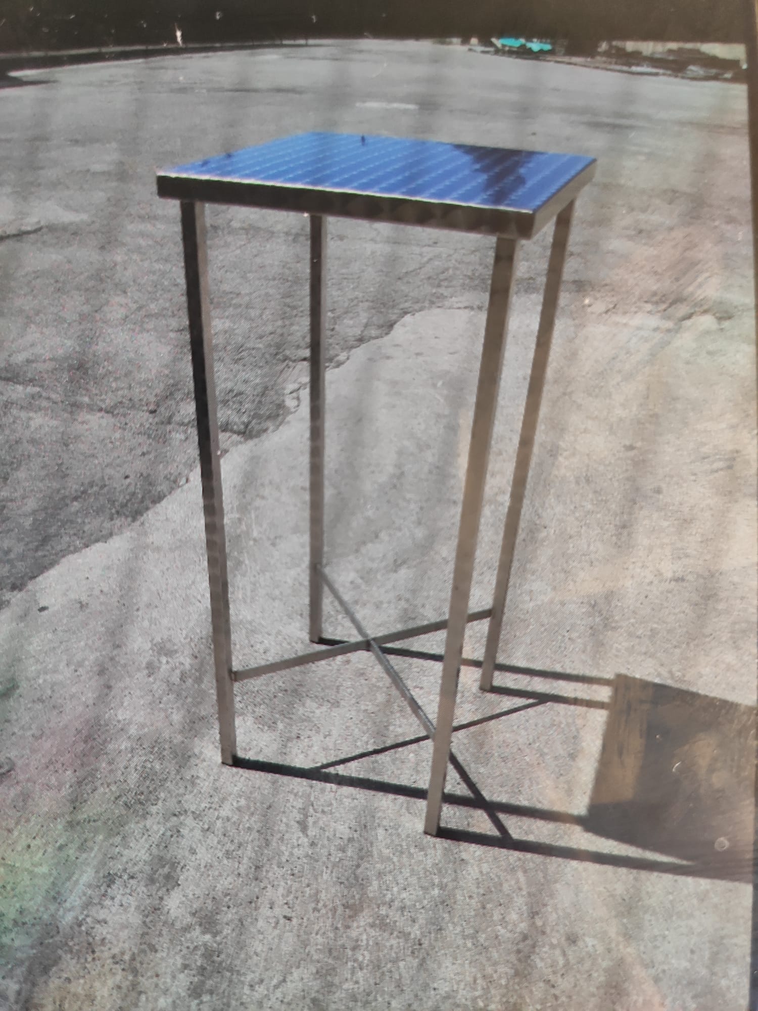 Supporto per piante in acciaio inox con piano quadrato, gambe collegate da supporti a X. Per esterni su cemento.