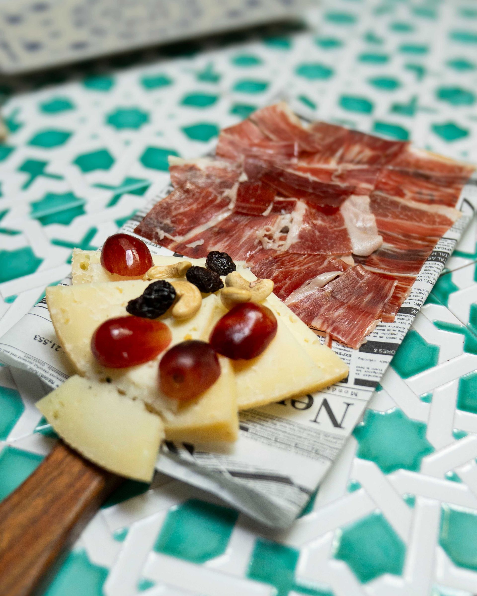 Tabla de embutidos con lonchas de carne curada, queso, uvas y aceitunas en una bandeja decorada.