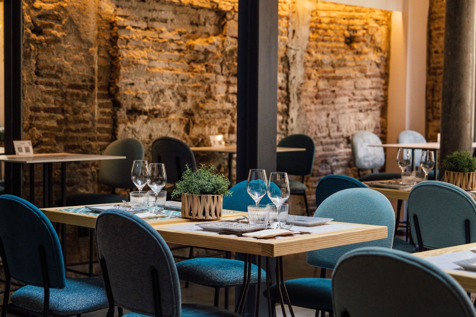Comedor de restaurante moderno con sillas color turquesa, mesas puestas y paredes de ladrillo cálido.