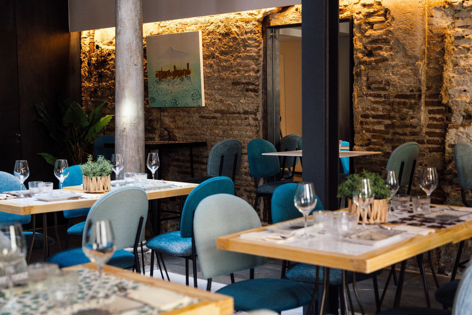 Elegante zona de comedor de restaurante con sillas azules, mesas puestas y una cálida iluminación ambiental.