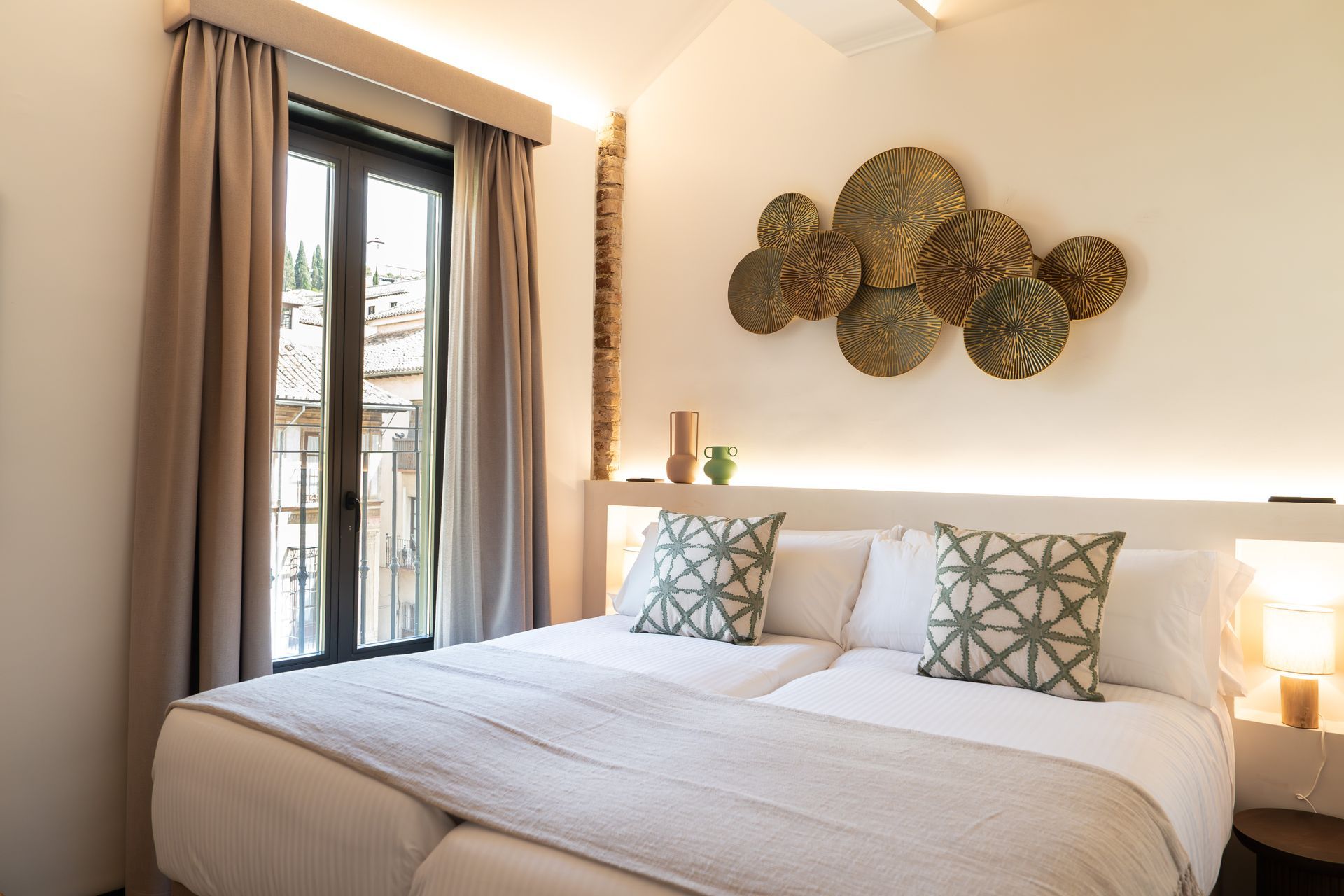 Habitación luminosa con una cama grande, cortinas grises y un cuadro decorativo sobre el cabecero.