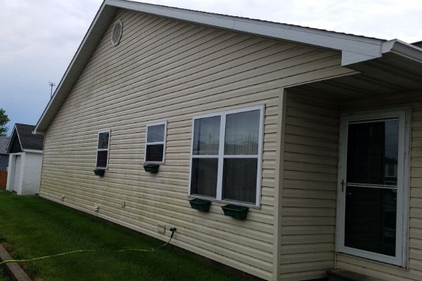 Side view of a beige house with vinyl siding, windows, and a screened porch door under a cloudy sky
