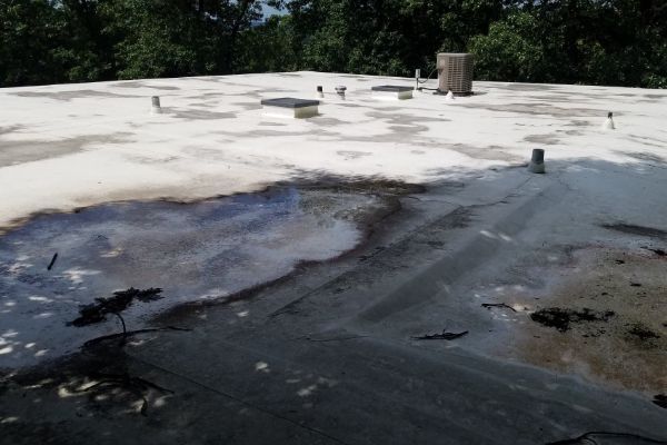 Foam-covered industrial surface with dark runoff and a small plume of smoke or steam near trees