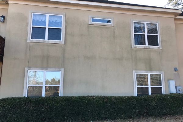 Two-story beige stucco house with white-trim windows and a trimmed hedge in front.
