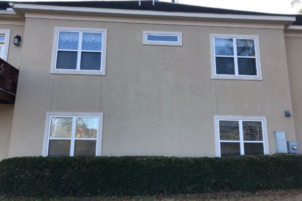 Two-story beige house facade with four windows and a hedge in front