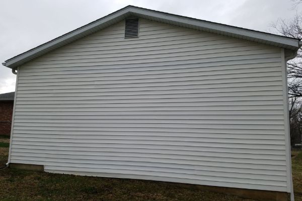 White vinyl-sided house exterior with a gray roof and small grass yard under an overcast sky