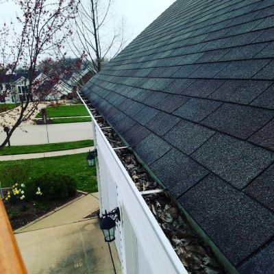 Gutter beside a dark shingled roof above a sidewalk and green lawns in a residential neighborhood