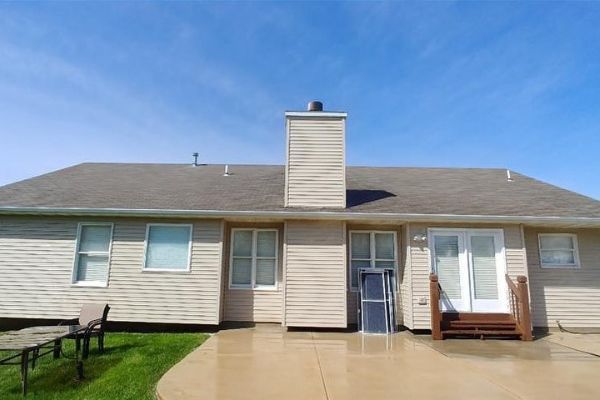 Back exterior of a beige townhouse with patio, sliding doors, and central chimney under a blue sky