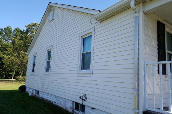 White vinyl-sided house exterior with a small porch and grassy yard on a sunny day