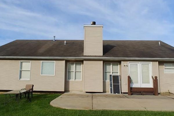 Single-story beige house with a central chimney, white windows, and a small patio in front.