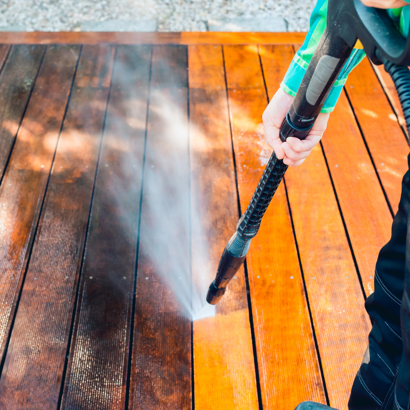 Cleaning a wooden deck with a pressure washer, spraying water on dark and orange planks