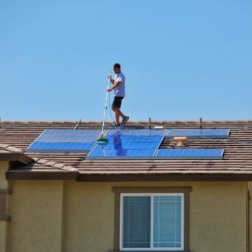 Person installing solar panels on a house roof on a sunny day