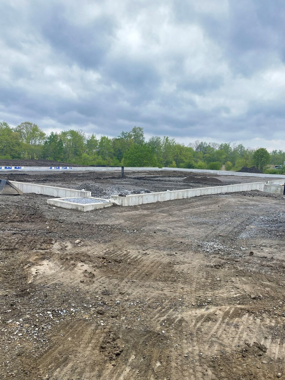 Construction site with dirt clearing, concrete foundation forms, and cloudy sky in the background