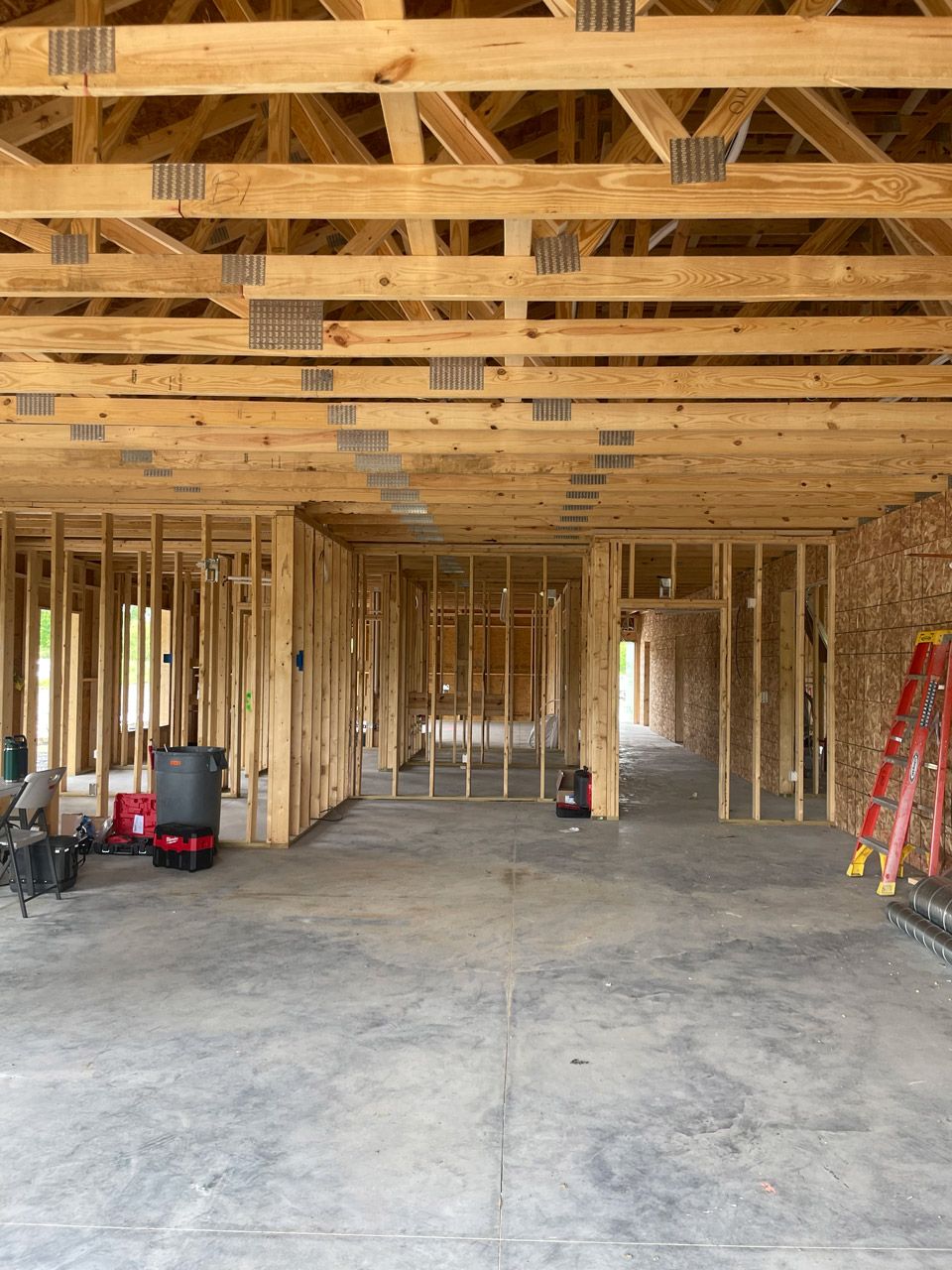 Unfinished house interior with exposed wood framing, concrete floor, and construction tools.