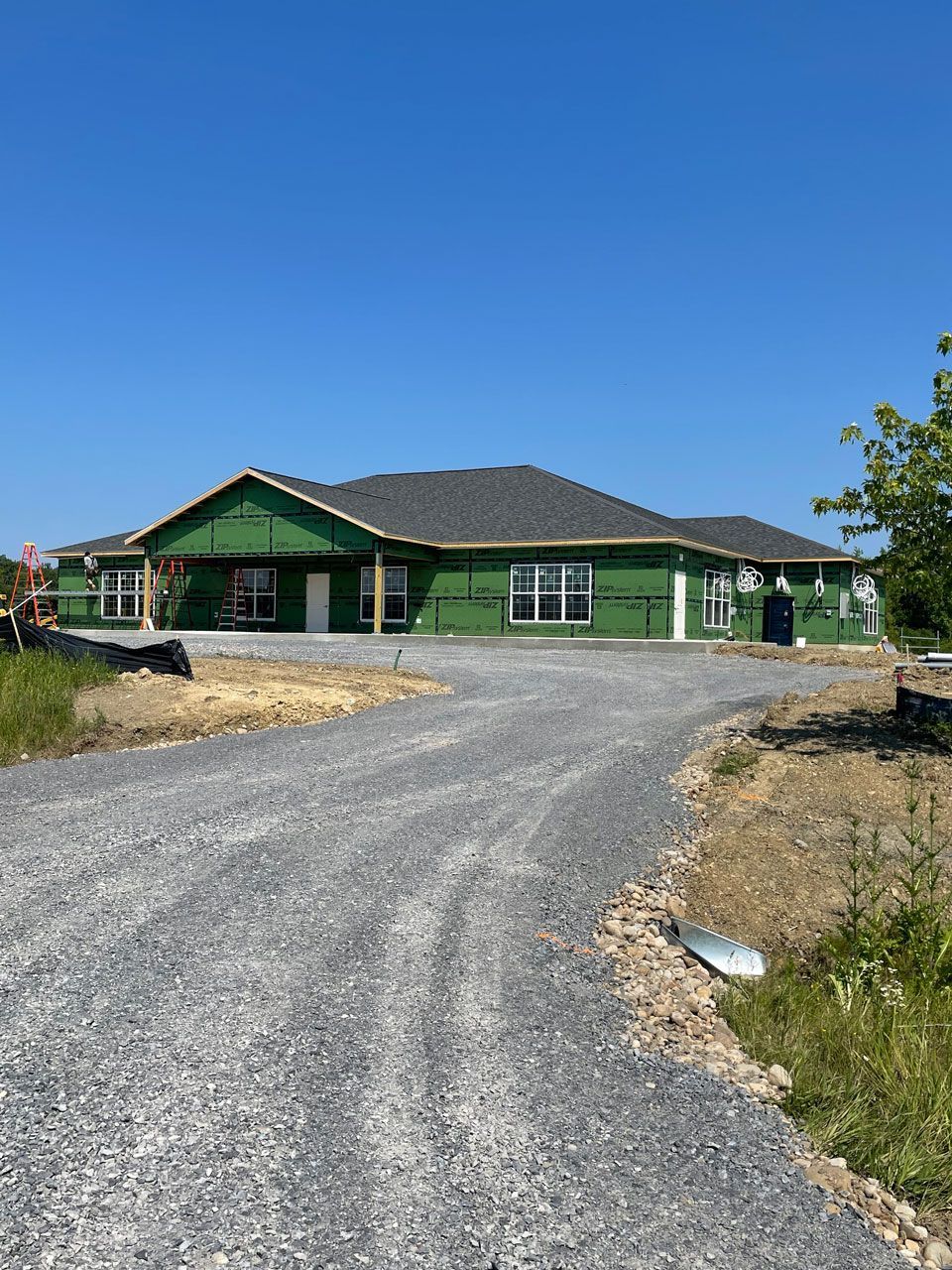 Green house with dark roof and gravel driveway under a clear blue sky.