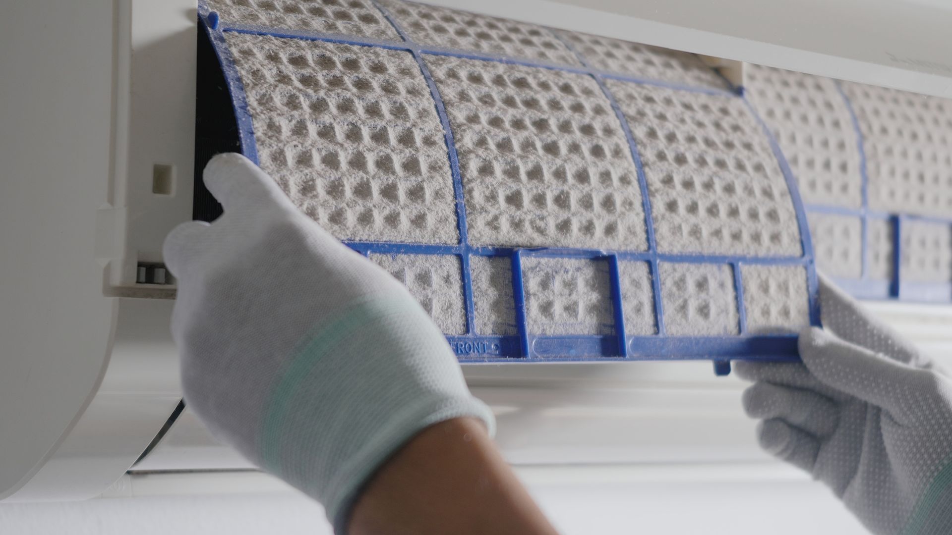 A person wearing white gloves is cleaning an air conditioner filter.