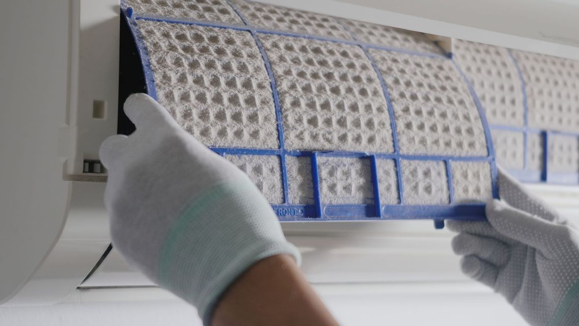 A person wearing white gloves is cleaning an air conditioner filter.