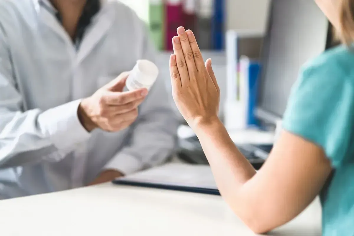 Doctor holding medicine bottle while speaking to a patient with raised hand in a clinic