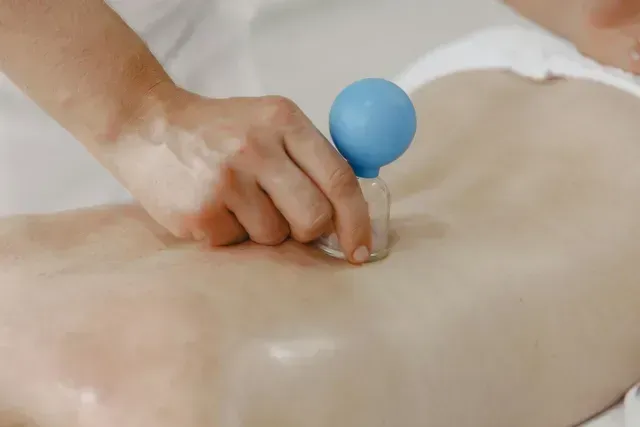 Hand pressing a blue suction cup onto a person’s bare back during a massage or therapy session