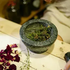 Stone mortar filled with green herbs on a tabletop, with dried red petals nearby
