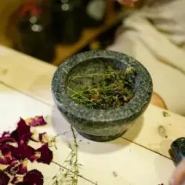Stone mortar filled with green herbs on a tabletop, with dried red petals nearby