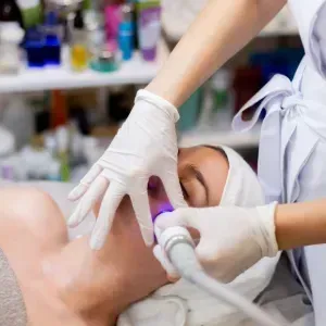 Gloved clinician using handheld device on a patient lying on a treatment bed in a spa clinic