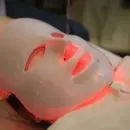 White LED face mask on a person lying down, glowing red in a spa setting
