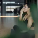 Person sitting on a mat, wiping sweat from their face in a gym or studio.