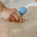 Hand pressing a small blue tool into a person's back during massage therapy