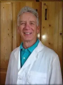A man wearing a white lab coat and a blue shirt is smiling for the camera.