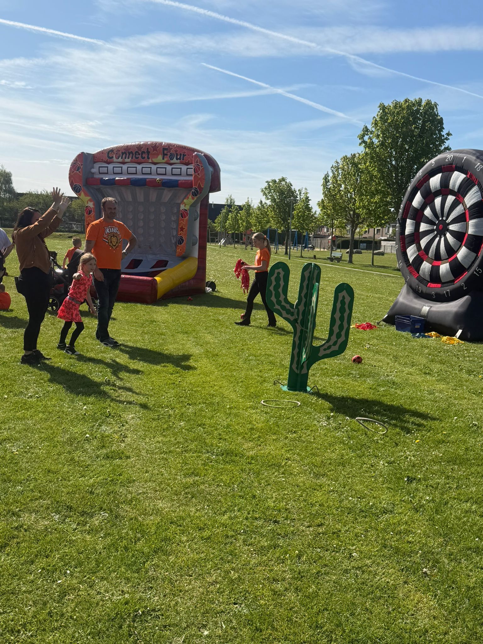 Een openlucht speelveld met een cactusdoel, een opblaasbaar dartbord en mensen die spelen op een zonnig gazon.