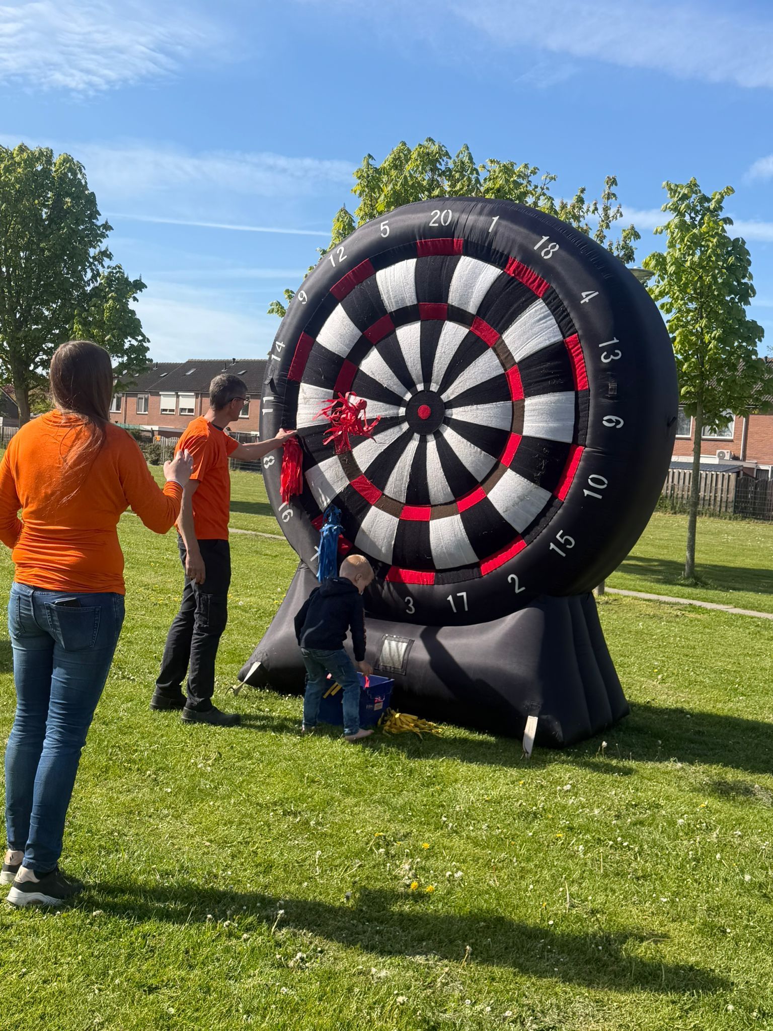 Mensen zetten een groot, zwart, wit en rood opblaasbaar dartbord buiten op het gras op.