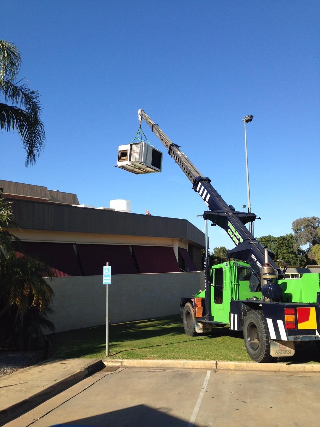 A Green Truck With A Crane Attached To It And Lifted An Air Conditioner — Custom Air In East Albury, NSW