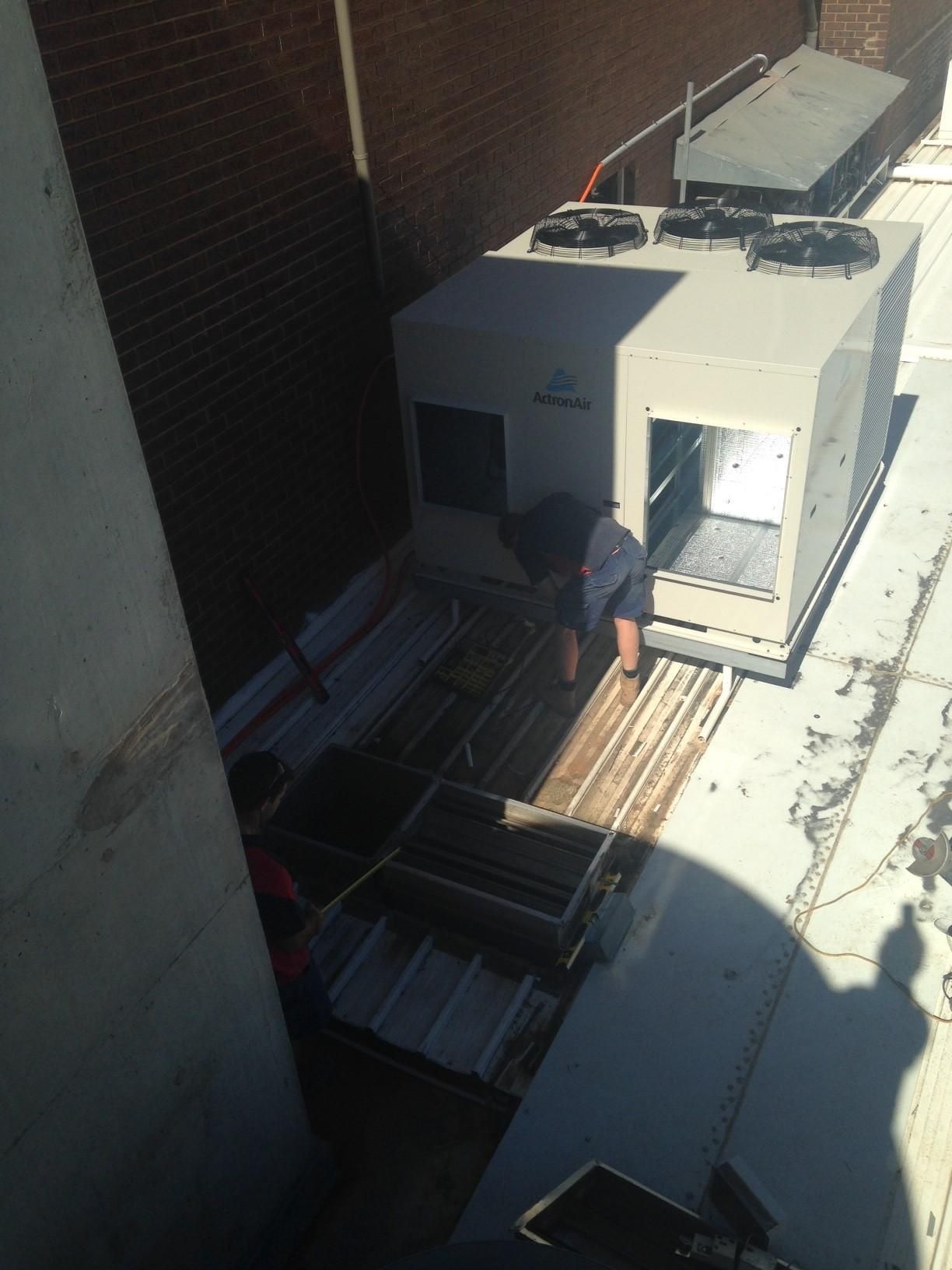 A Man Is Installing An Aircondition On The Roof Of A Building — Custom Air In Wodonga, NSW