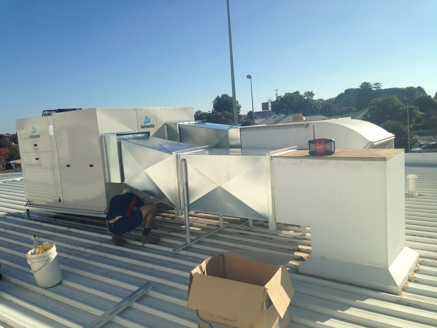 A Man Is Working On A Machine On The Roof Of A Building — Custom Air In East Albury, NSW