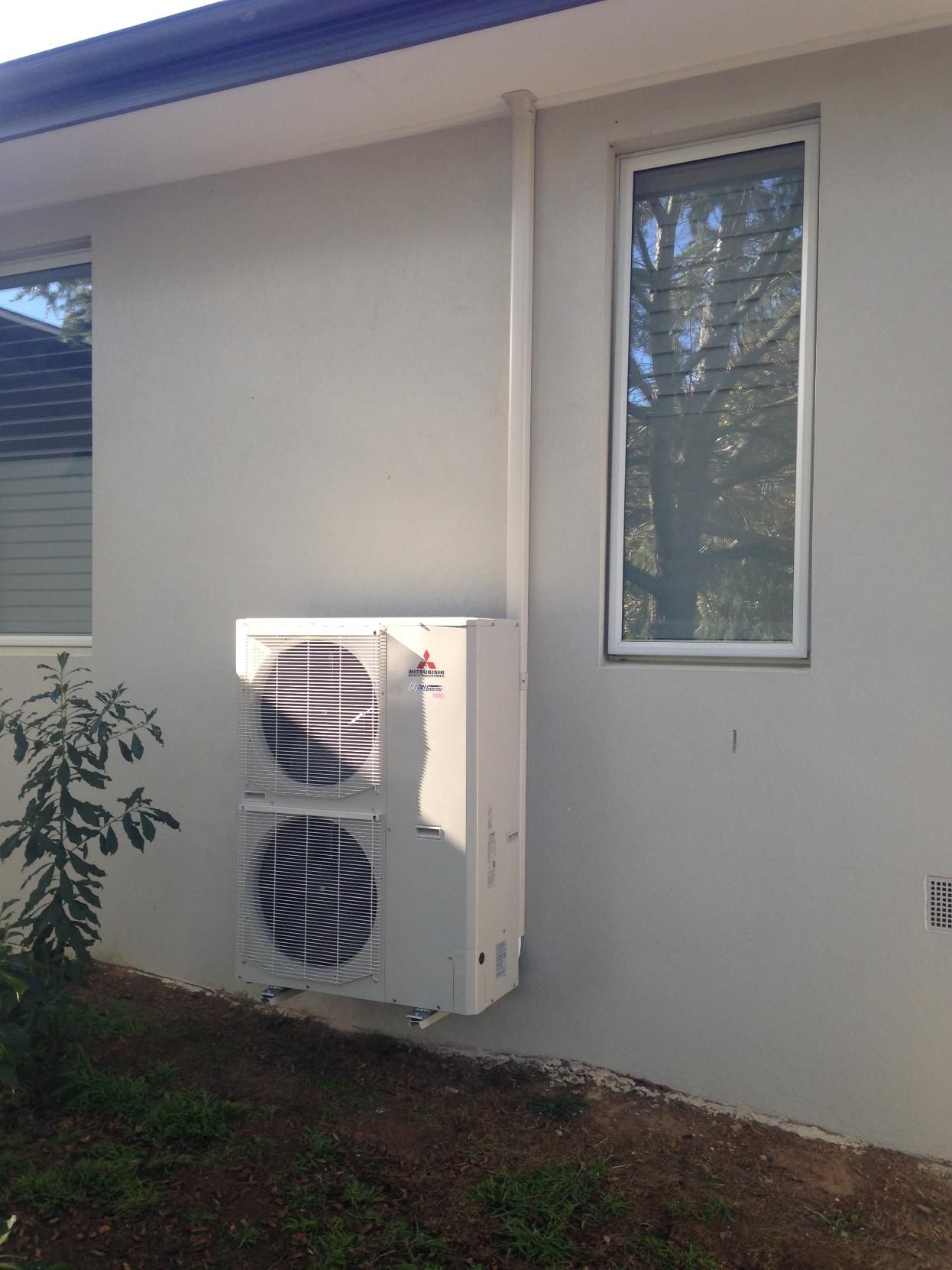 A Large Air Conditioner Is Mounted On The Side Of A House Next To A Window — Custom Air In Wodonga, NSW
