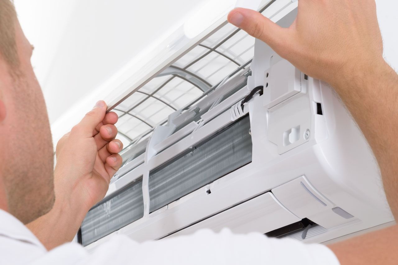 A Man Is Fixing An Air Conditioner On A Wall — Custom Air In East Albury, NSW