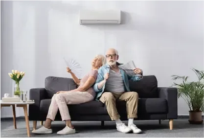 Two people relaxing on a dark sofa in a bright living room with a wall-mounted air conditioner.